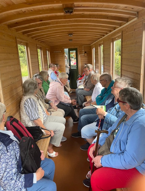 Blick durch einen schmalen Waggon des "Kaffeebrenner-Expresses ". Links und rechts sind längs der Wände Holzbänke, auf denen einige Teilnehmer und Teilnehmerinnen sitzen.